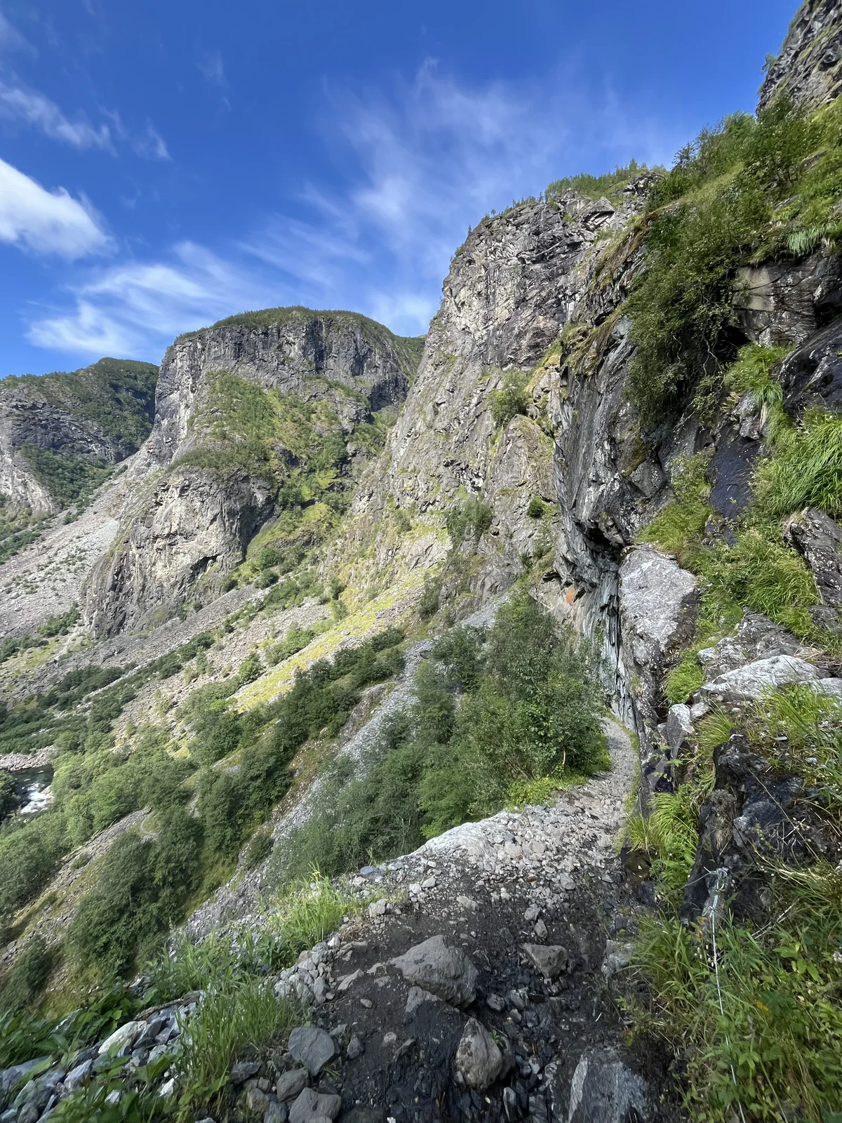 A narrow trail beside tall grey cliffs and green slopes in Norway